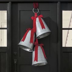 three bells hanging from the side of a black door with red ribbon on each one