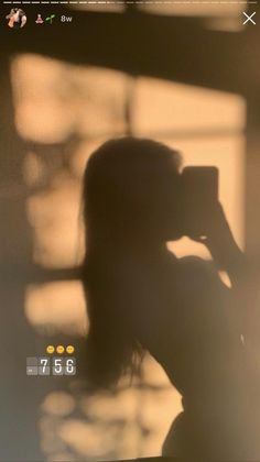 the silhouette of a woman taking a photo with her cell phone while standing in front of a window