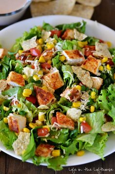 a salad with chicken, lettuce, corn and dressing on a white plate