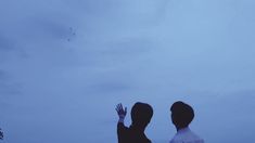 two people are flying a kite in the sky at dusk or dawn with their hands up