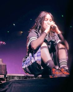 a woman sitting on top of a stage with her hands in her mouth and legs crossed