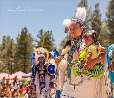 two women and a child in native american clothing at an outdoor event with other people