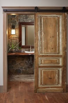 an open door leading to a bathroom with stone walls and wood floors, along with a sink