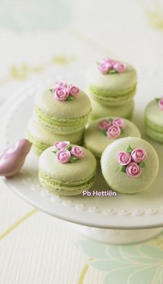 there are many green macaroons with pink flowers on them sitting on a plate