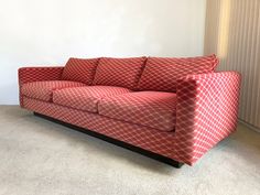 a red couch sitting on top of a carpeted floor next to a white wall