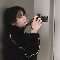 a woman holding a camera up to her face while leaning against a wall with the door open