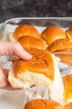 someone is dipping cheese on top of some buns in a baking dish with other rolls