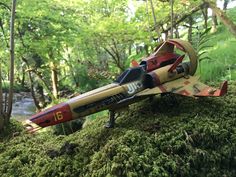 a toy airplane sitting on top of a moss covered rock in the woods next to a stream