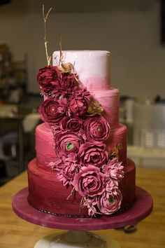 a three tiered cake with pink flowers on the top and purple frosting on the bottom