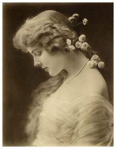 an old black and white photo of a woman with flowers in her hair wearing a dress