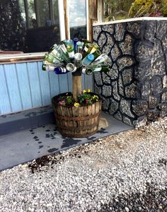 a wooden barrel filled with lots of bottles next to a stone wall and flower pot