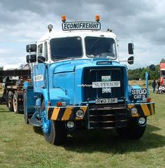 a large blue truck parked on top of a grass covered field next to other trucks