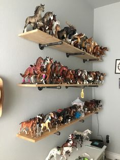 three wooden shelves filled with assorted toy horses on top of each other in a room