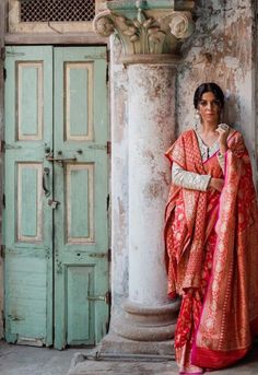 a woman in an orange and pink sari standing next to a tall column with two doors