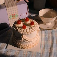 a white cake with cherries on top sitting next to a cup and saucer