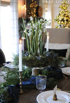 the table is set for christmas with candles and greenery on it, along with other holiday decorations