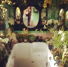 a bath tub sitting next to a mirror in a room filled with plants and flowers