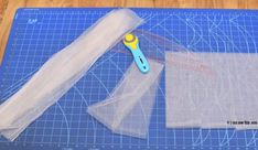 a pair of scissors sitting on top of a blue cutting mat next to a piece of clear plastic