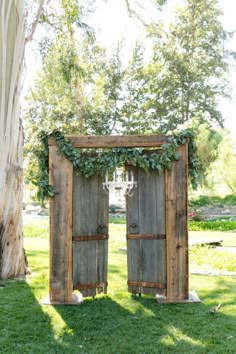 two wooden doors with vines on them are in the grass next to a large tree