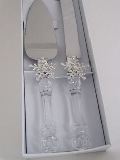 two clear candlesticks in a white box with flowers on each one and a knife