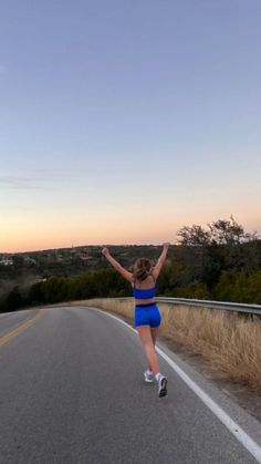 a woman running down the road with her arms in the air