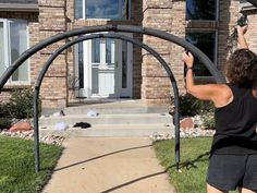 a woman is holding up an arch in front of a house with a cat laying on the sidewalk