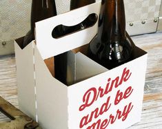 two beer bottles in a white box with the words drink and be merry written on it