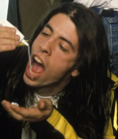 a man with long hair brushing his teeth while sitting in a chair next to another person