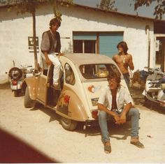 two men sitting on the back of an old car in front of a white building