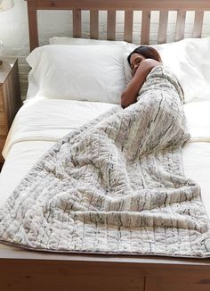 a woman laying in bed under a blanket on top of a wooden headboard and foot board