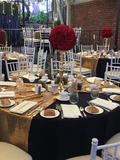 the tables are set with gold and black linens, white chairs, red roses, and silverware