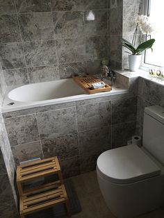 a white toilet sitting next to a bath tub in a bathroom with gray tile on the walls