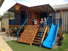 two children are playing in the backyard with a slide and play set on grass area