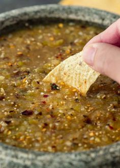 a hand dipping a tortilla chip into a bowl of soup