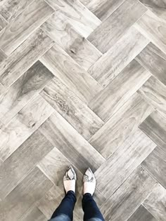 a person standing on top of a wooden floor next to a white wall and gray tile