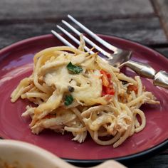 a pink plate topped with pasta covered in sauce and vegetables next to a fork on top of a wooden table