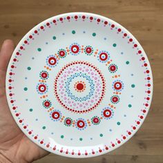 a hand holding a white plate with multicolored circles and dots on the rim