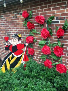 a brick wall with red roses growing next to it and a cartoon character painted on the side