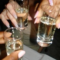 several people are holding up glasses with liquid in them and one person has their hand on the glass