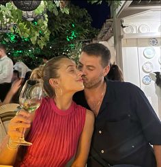 a man and woman kissing while holding wine glasses