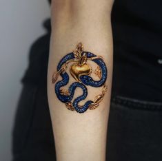 a tattoo on the arm of a woman with a gold heart and blue snakes around it