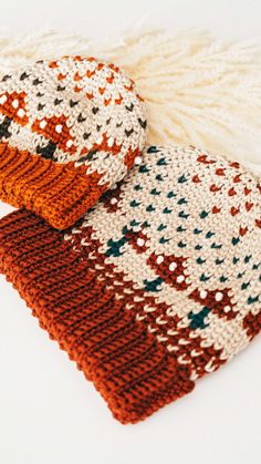 two knitted scarves sitting next to each other on top of a white table