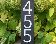 a black and white house number sign in front of green plants