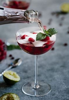 someone is pouring something into a glass with ice and raspberries