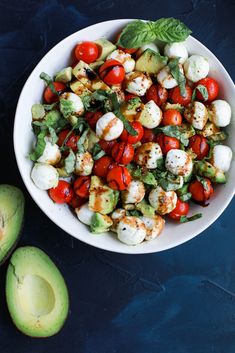 a white bowl filled with tomatoes, mozzarella and other toppings next to an avocado