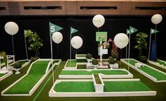 an indoor miniature golf course with white balloons and green grass in the center, on display