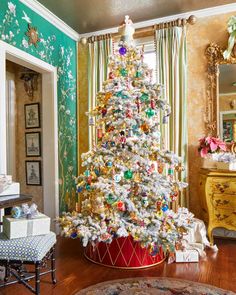 a decorated christmas tree in a living room next to a dresser and window with curtains