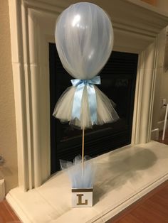 a white balloon with a light blue ribbon tied to it sitting in front of a fireplace