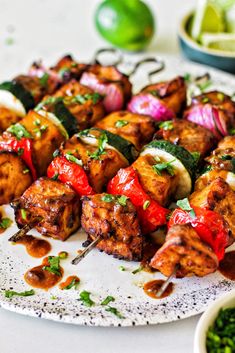 chicken and vegetable kabobs on a white plate with green garnishes