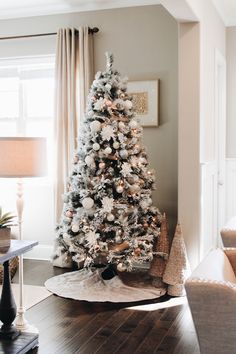 a white christmas tree in the corner of a living room with a window behind it